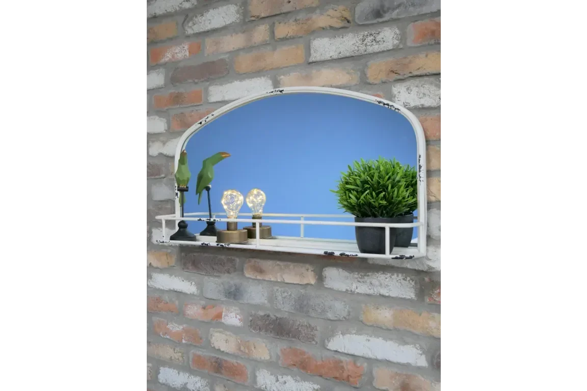 Arched wall mirror with white metal frame and shelf holding decor and artificial plant