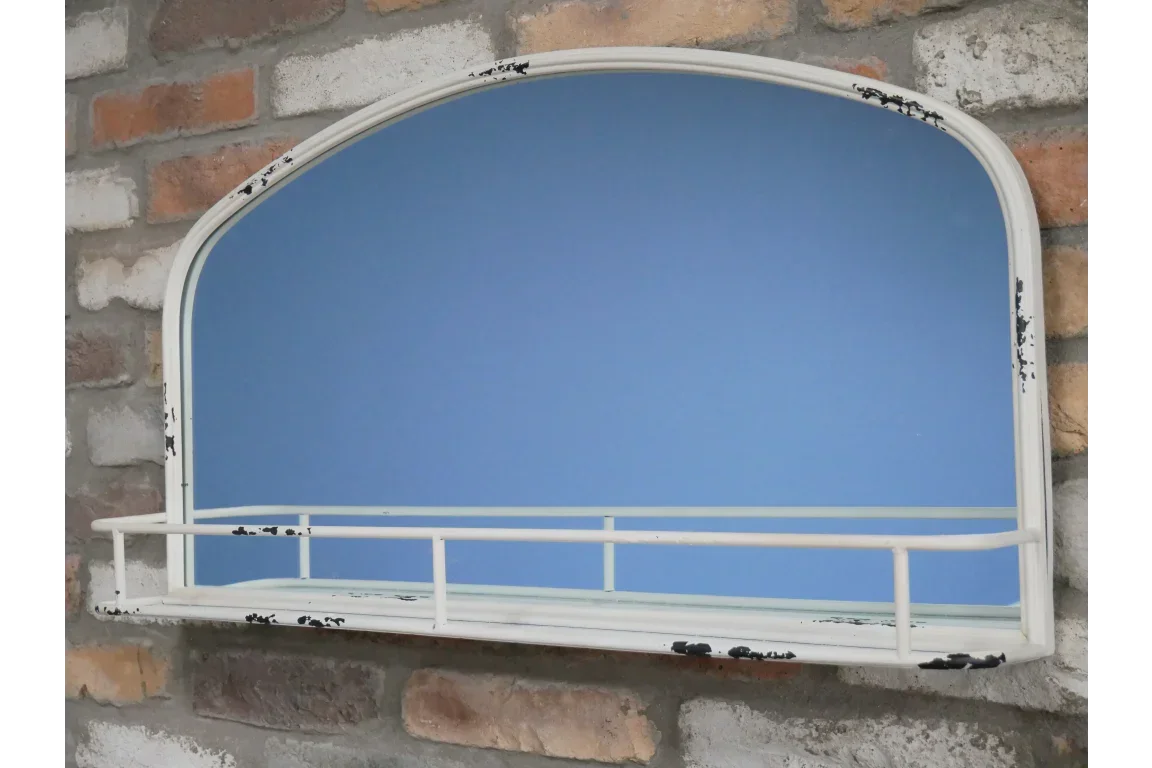 Arched wall mirror with distressed white metal frame and shelf mounted on brick wall