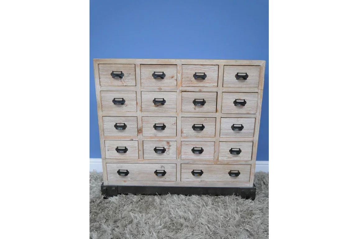 Distressed wood chest of drawers with black handles on shaggy rug against blue wall
