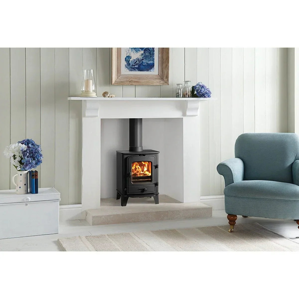 Black wood burning stove in white fireplace with blue armchair in cosy living room