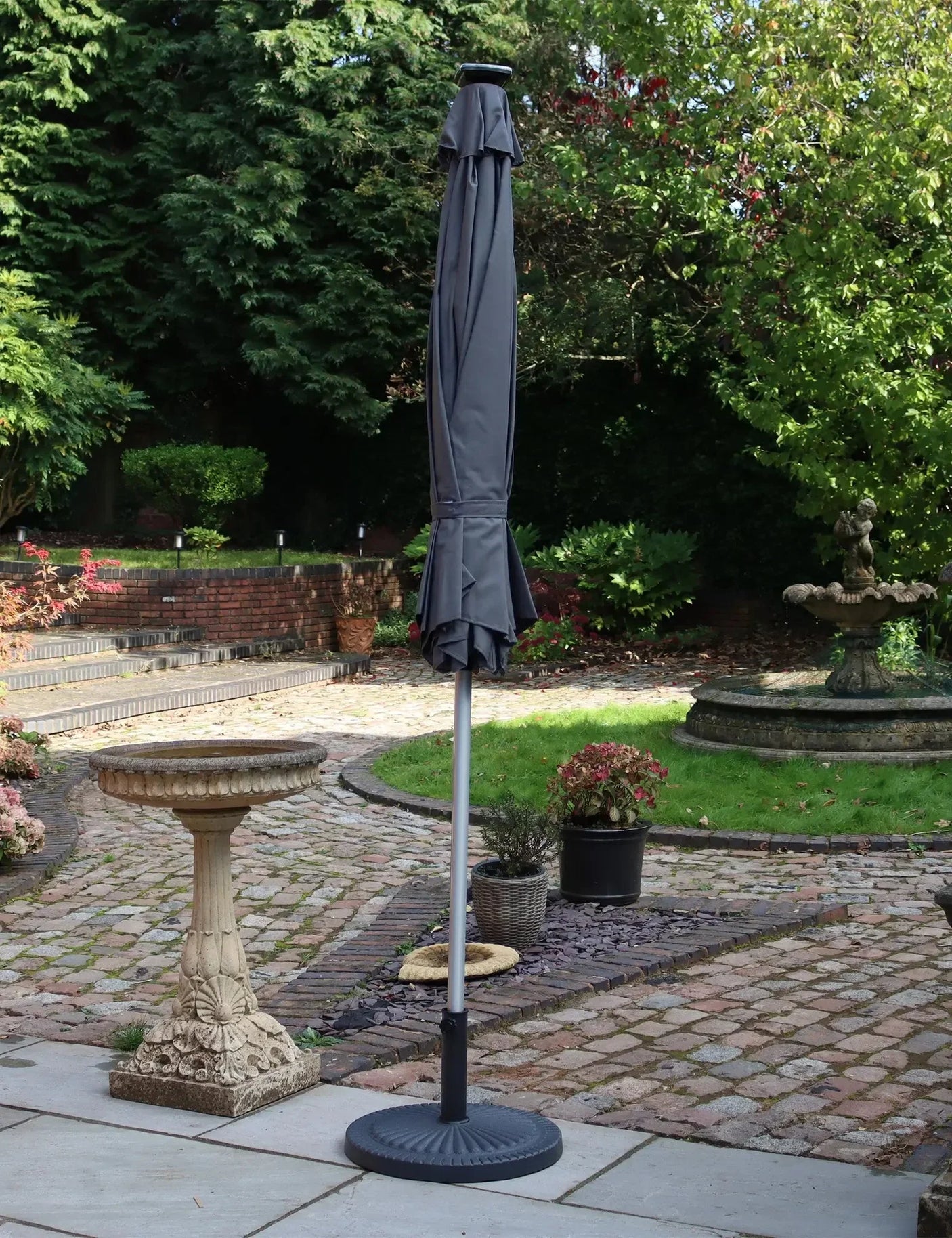 Grey garden parasol with metal pole and base on stone patio in landscaped backyard