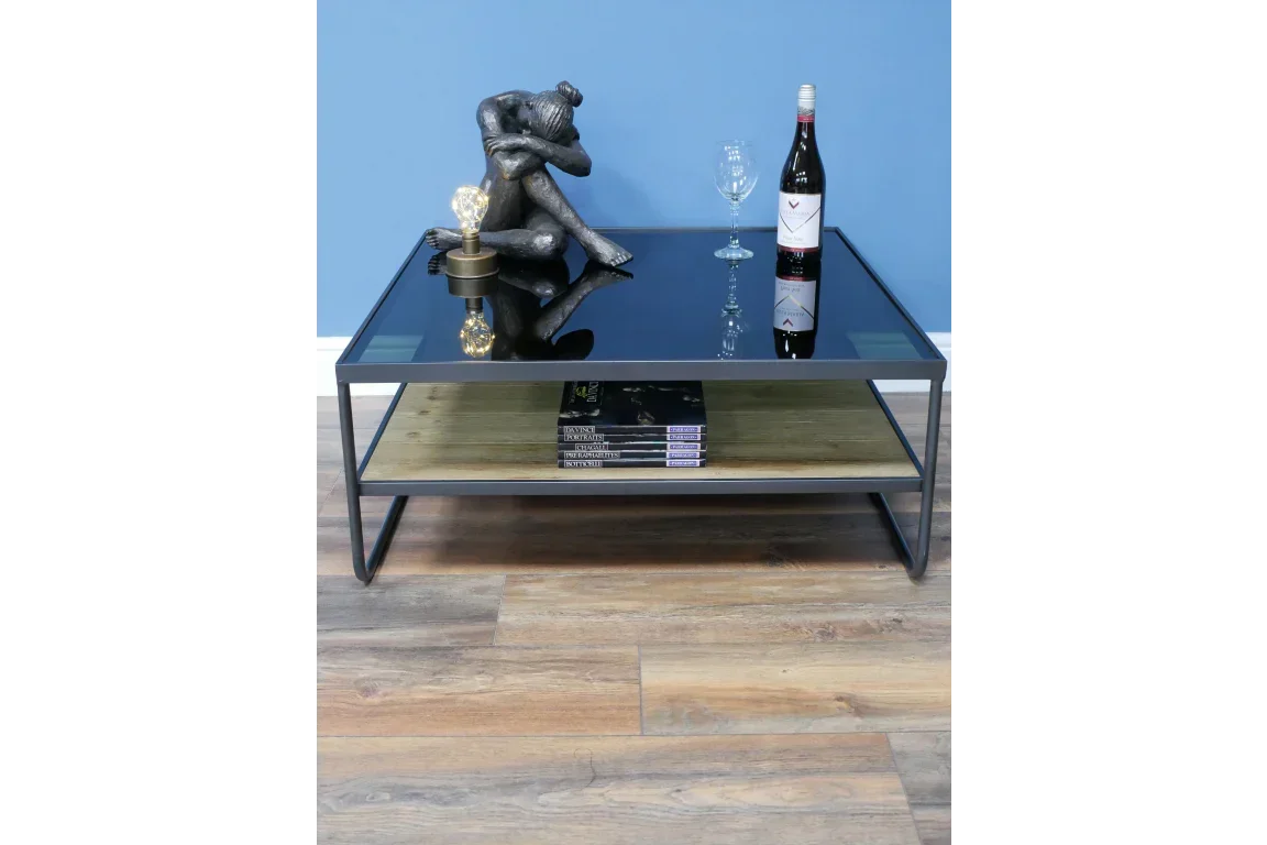 Modern glass coffee table with black frame, decorative sculpture, wine bottle, and shelf books