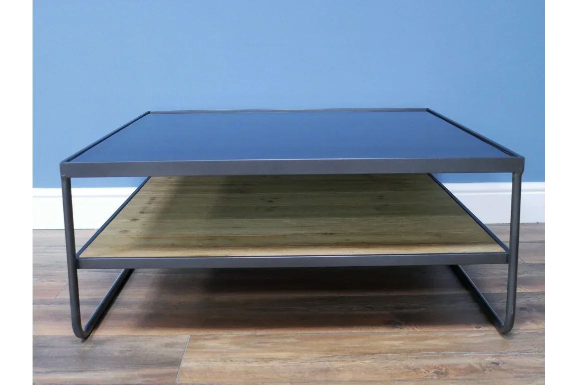 Modern coffee table with black metal frame, glass top, and wood shelf on hardwood floor