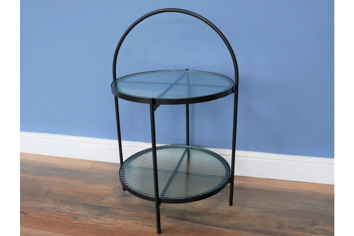 Round glass side table with black metal frame and two shelves on wood floor