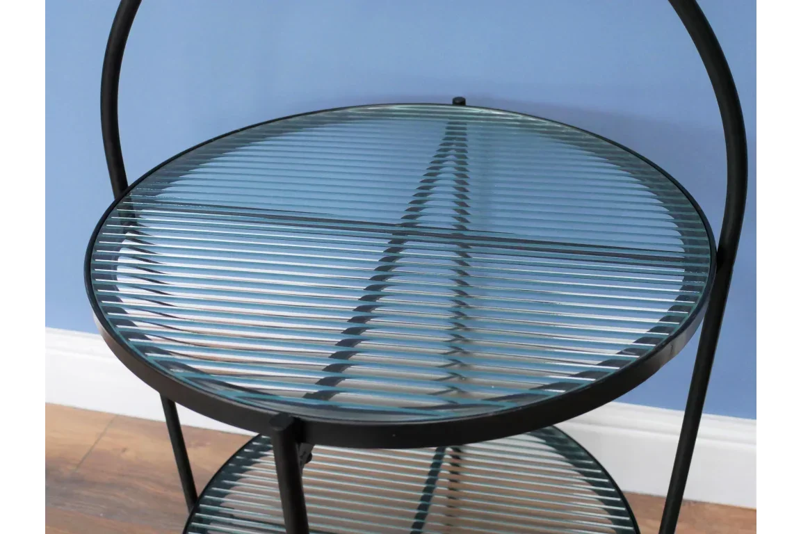 Round glass side table with black metal frame and ribbed shelves against blue wall