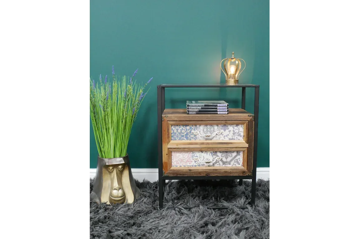 Rustic wooden bedside table with patterned drawers, metal frame, books, and lamp
