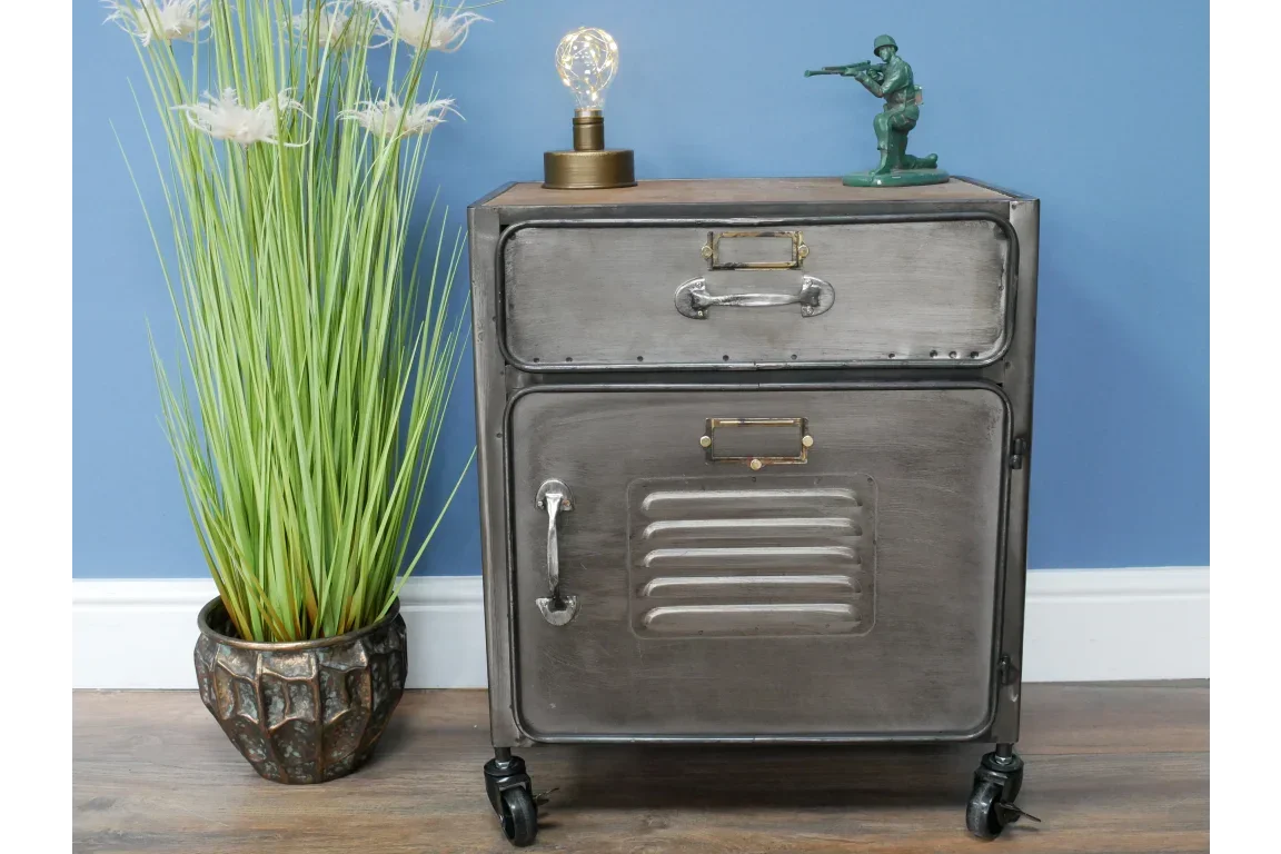Industrial metal bedside cabinet with drawer and door, set on caster wheels, next to plant