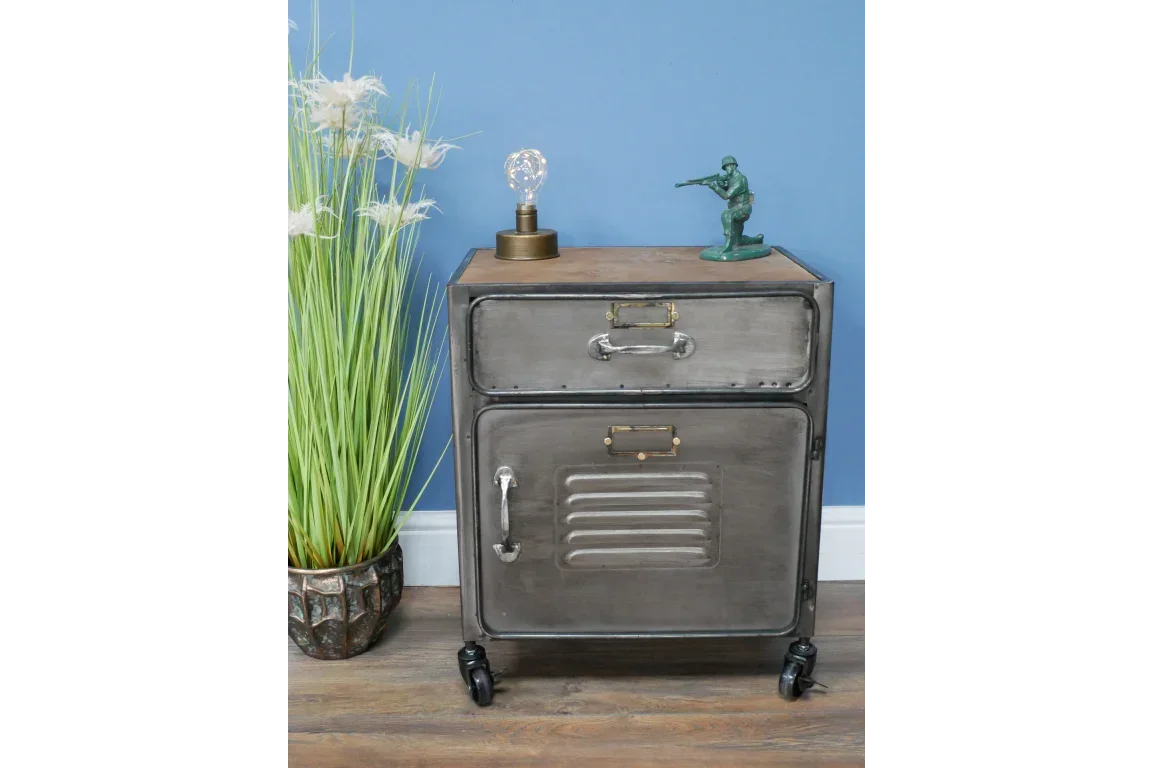 Industrial metal bedside cabinet with drawer and cupboard on castor wheels, against blue wall
