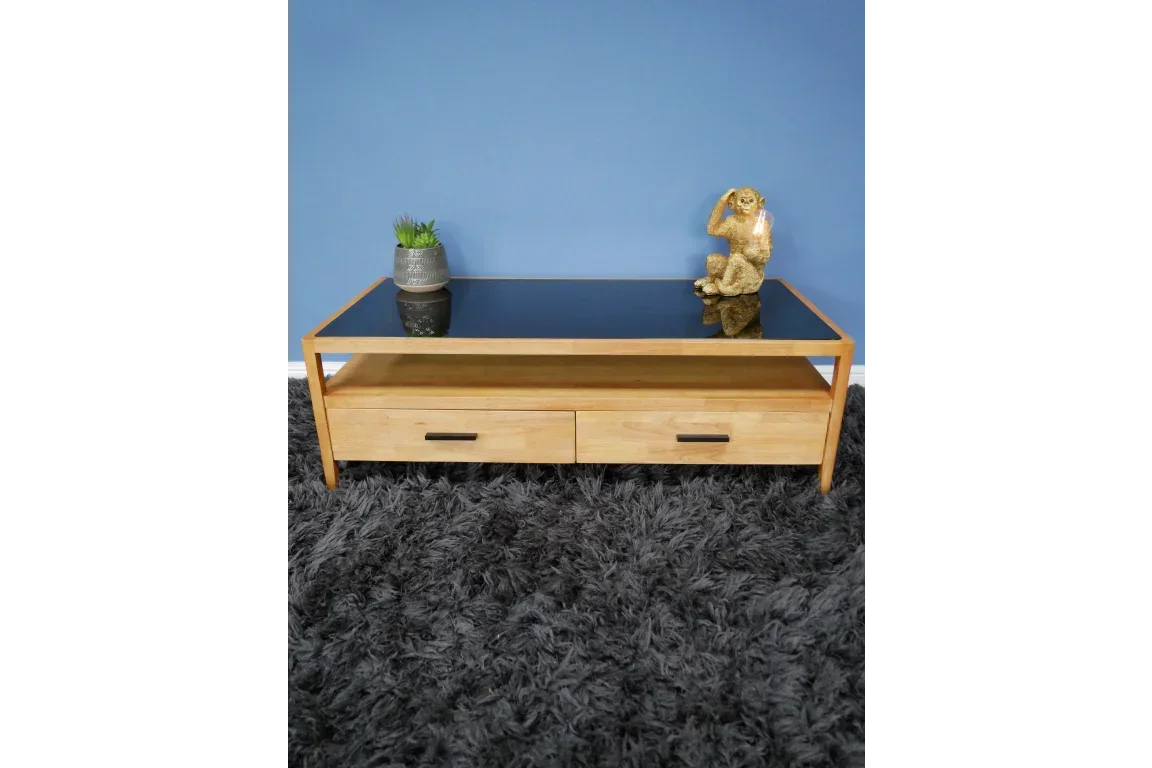 Modern oak coffee table with black glass top and two drawers on grey rug