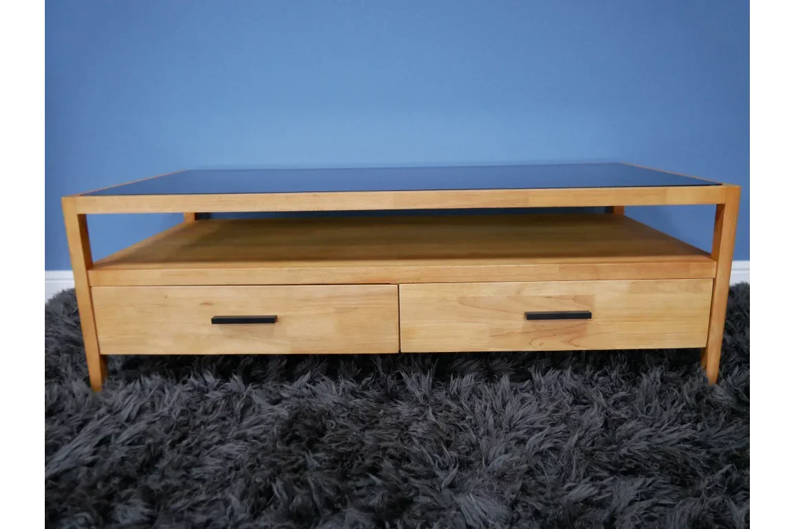 Wooden coffee table with two drawers and open shelf on grey rug against blue wall
