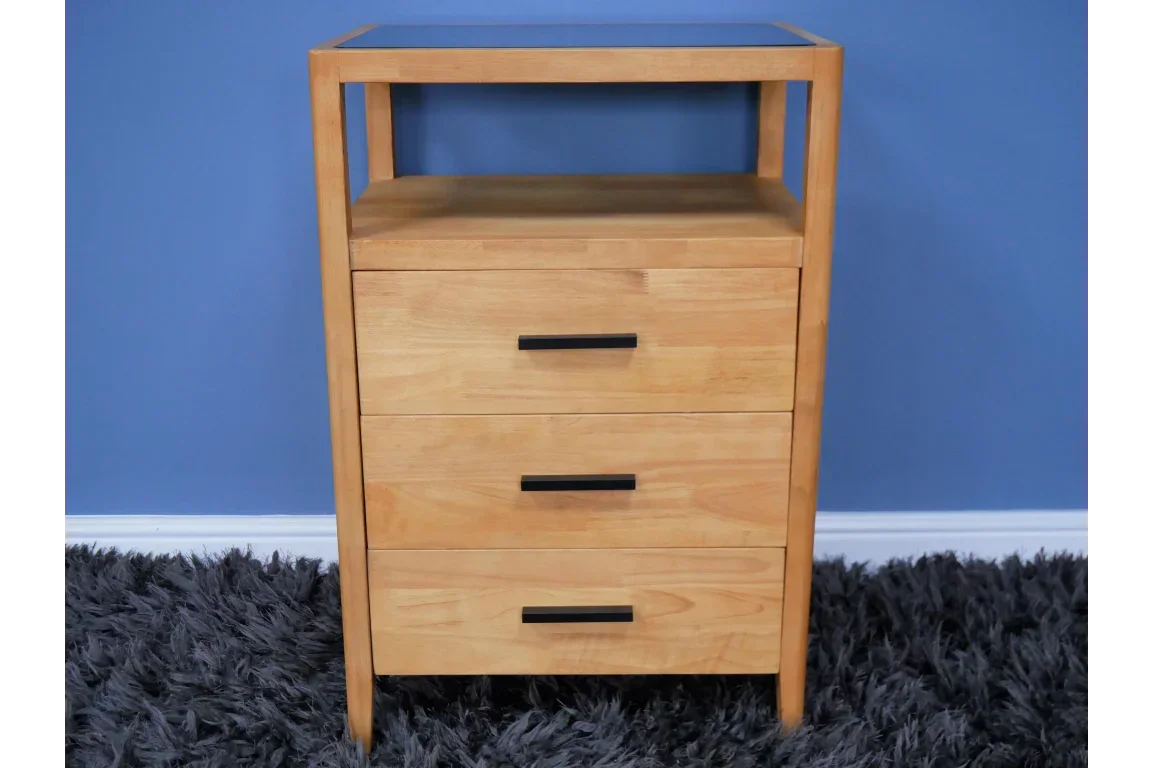 Light wood chest of drawers with black handles on grey rug against blue wall