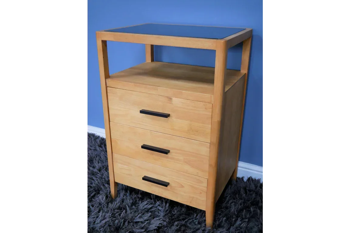 Light wood chest of drawers with black handles and open shelf on top, against blue wall