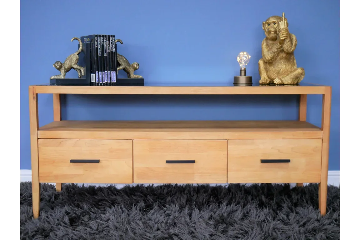 Light wood TV unit with three drawers, black handles, open shelf, styled with decor items