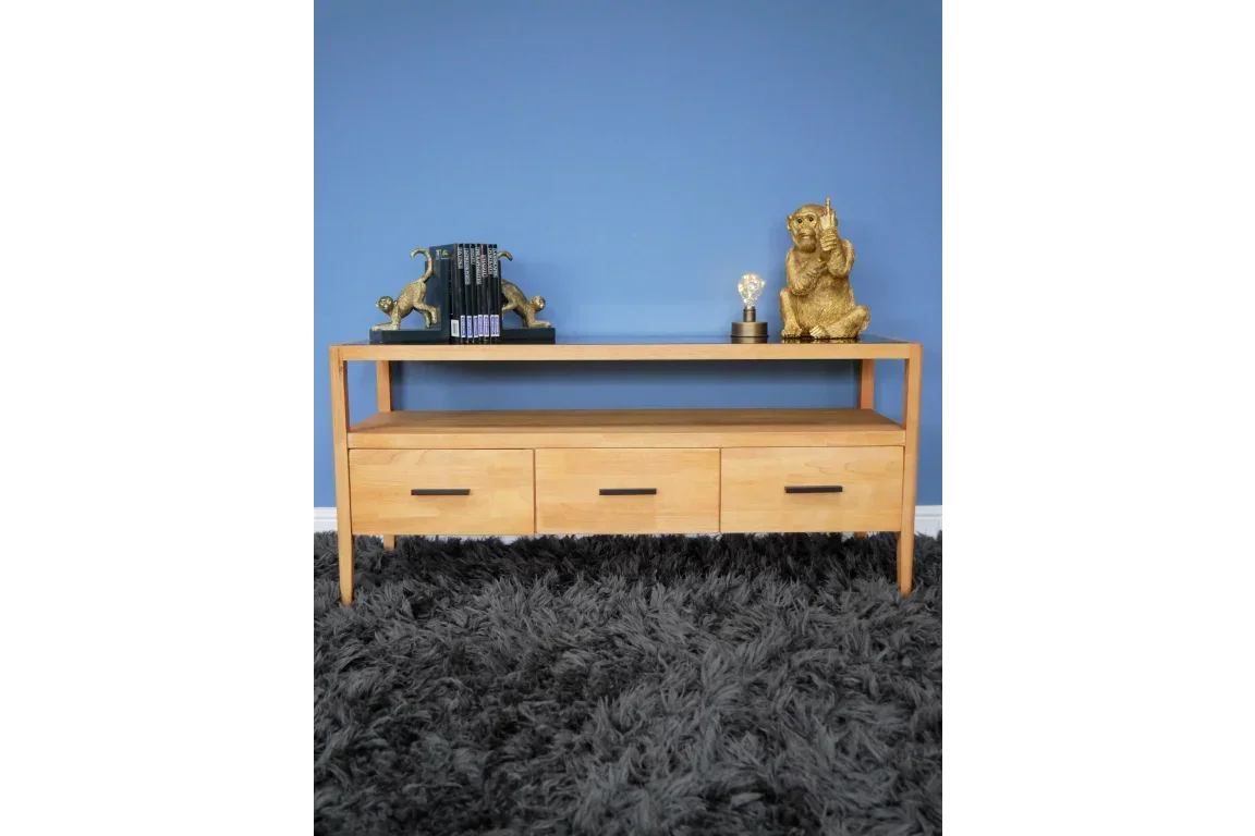 Light oak console table with three drawers and open shelf against a blue wall on grey rug