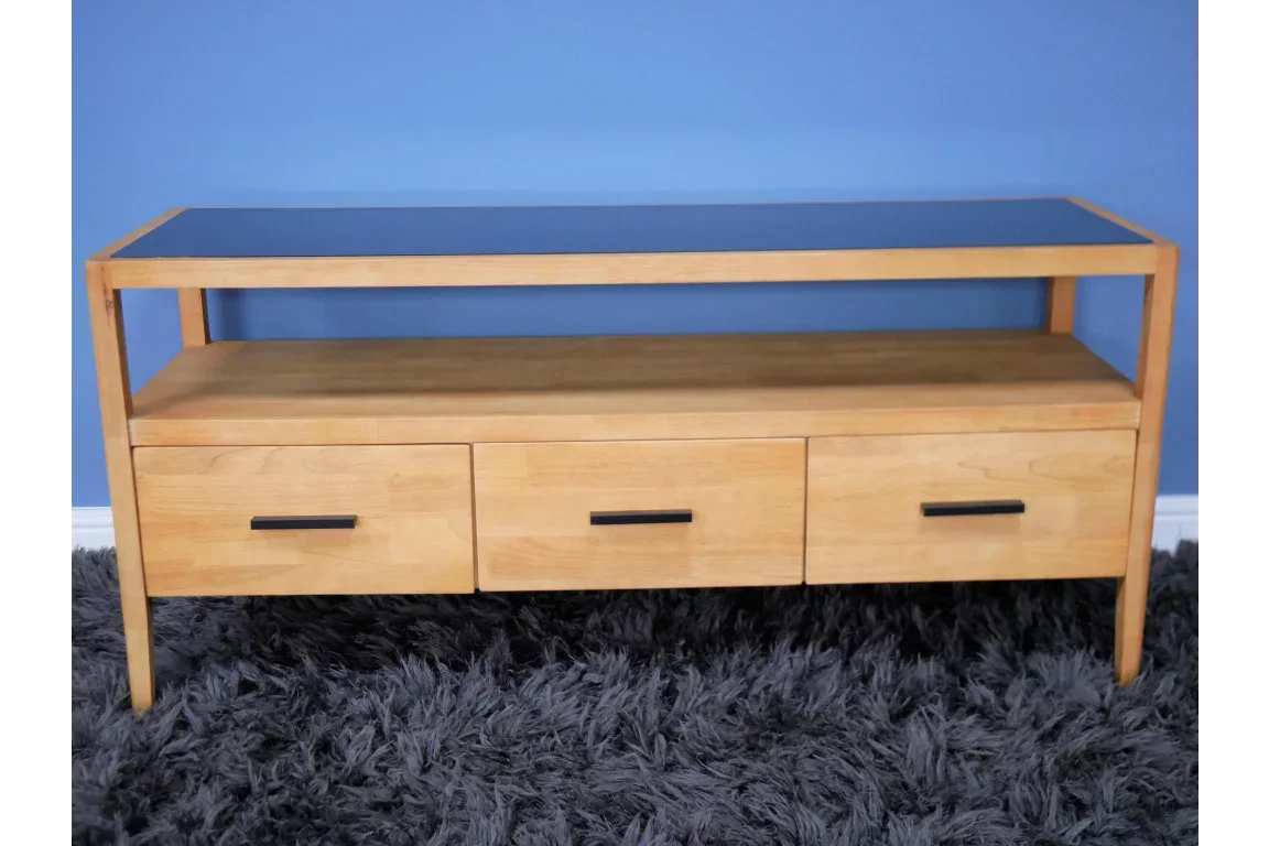 Wooden TV unit with three drawers and open shelf, black handles, on grey rug against blue wall