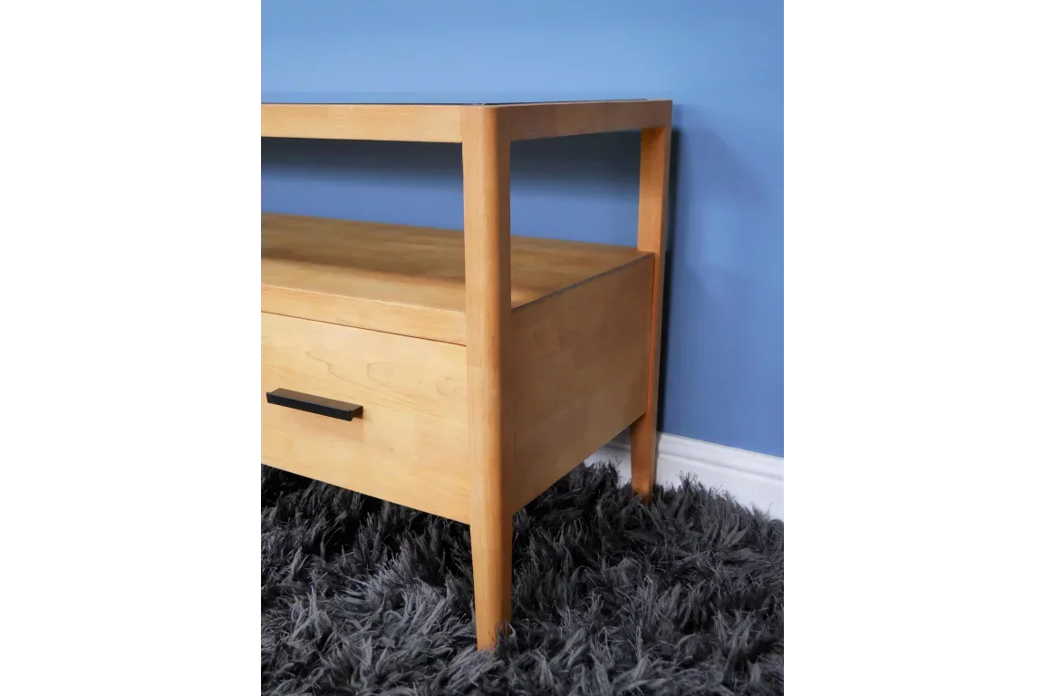 Light wood coffee table with drawer and black handle on grey rug against blue wall