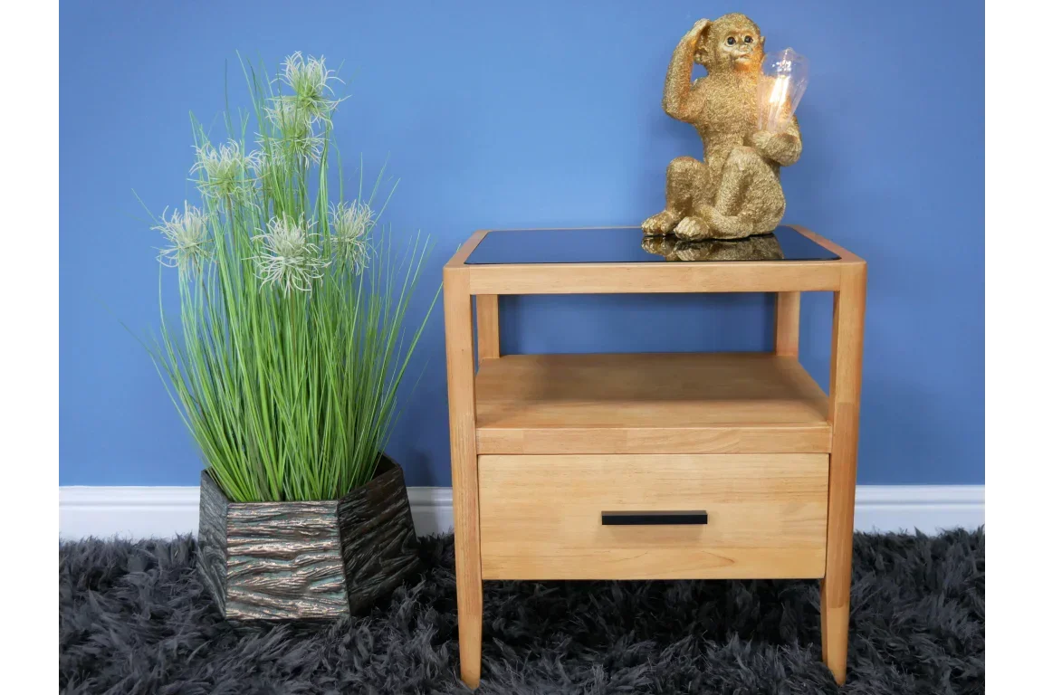 Oak bedside table with drawer and black glass top beside potted plant and gold monkey lamp