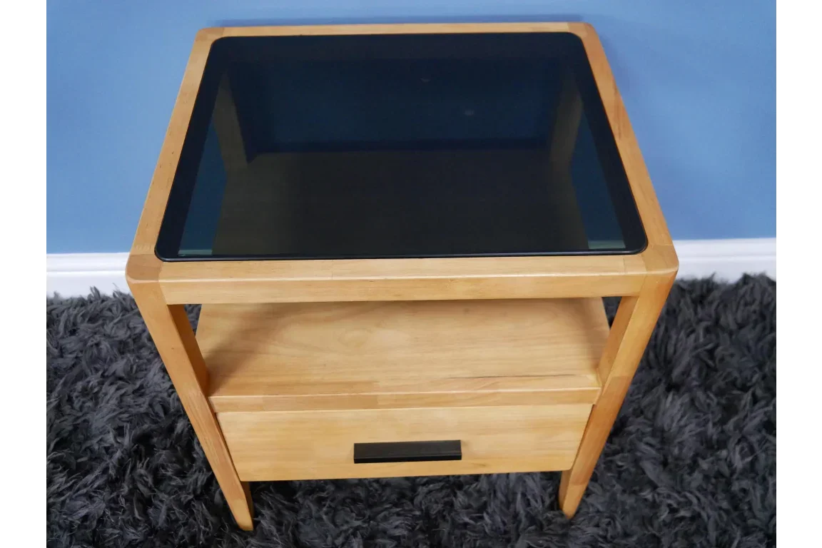 Wooden side table with black glass top, storage shelf and drawer, on grey rug