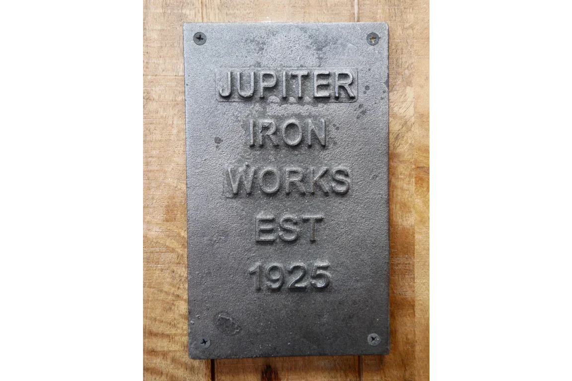 vintage cast iron wall plaque with embossed Jupiter Iron Works EST 1925 text on wood background
