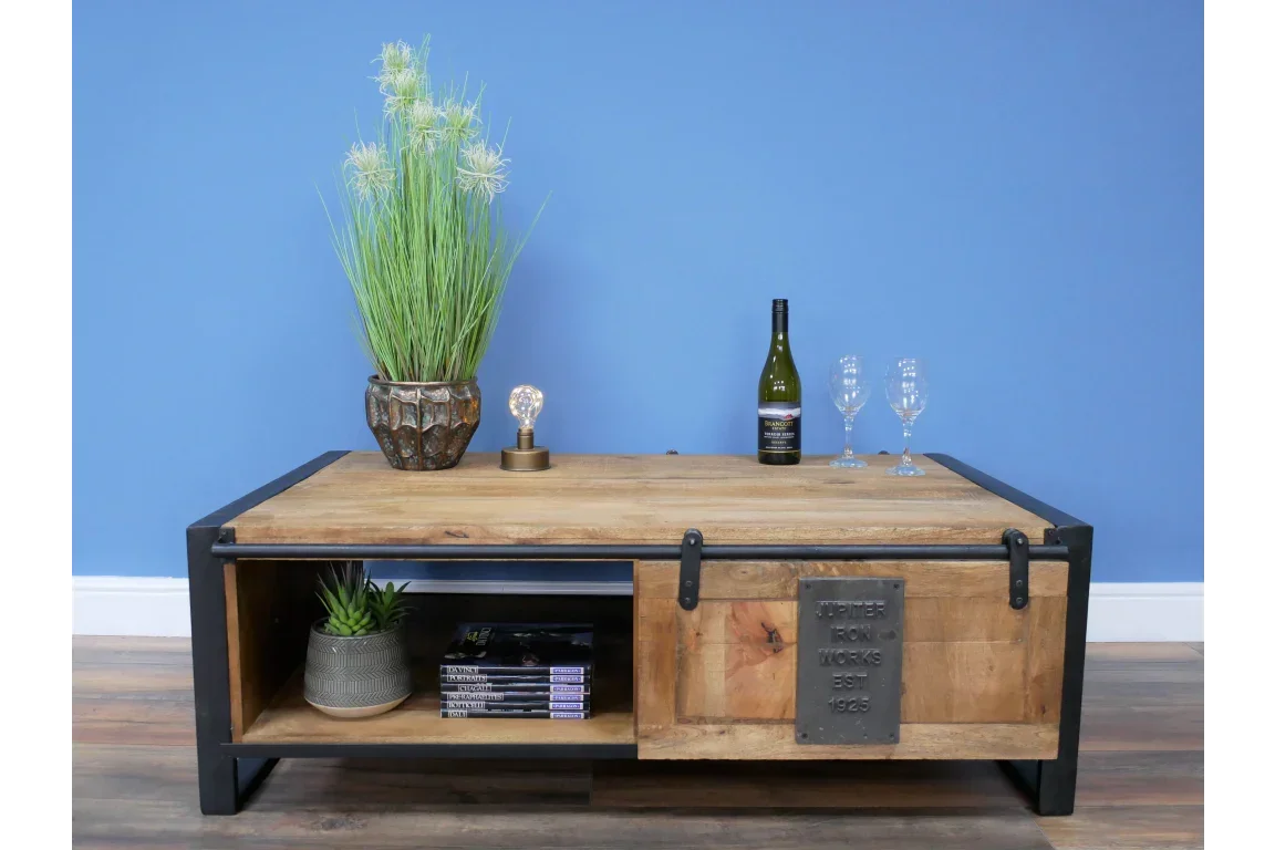 Industrial wood and metal coffee table with sliding door, wine glasses, and decorative plant