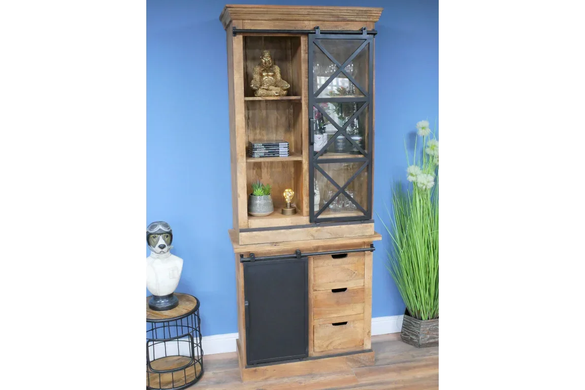 Tall wooden display cabinet with glass sliding door, shelves and drawers, against blue wall