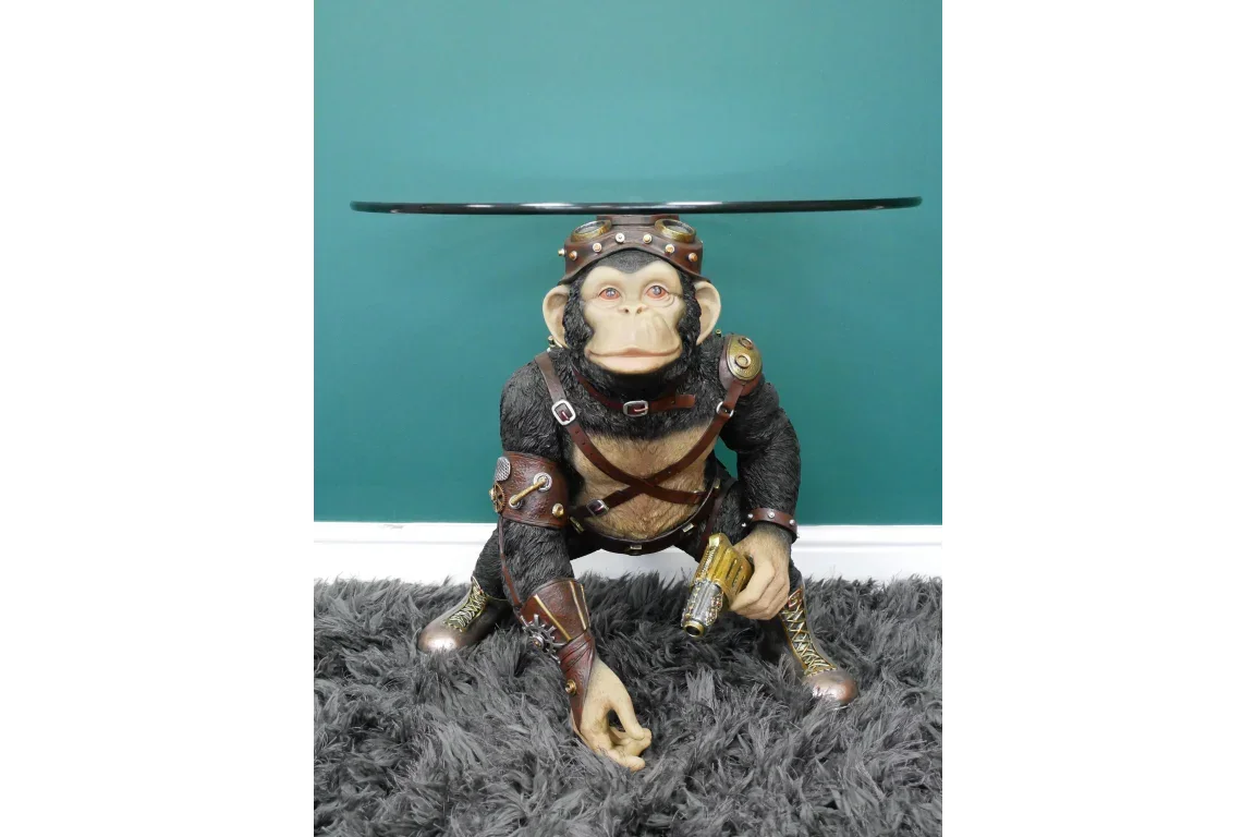Steampunk monkey side table with round glass top on grey rug against teal wall