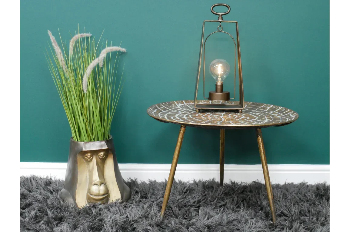 Round patterned metal side table with tripod legs and decorative lamp on shaggy rug
