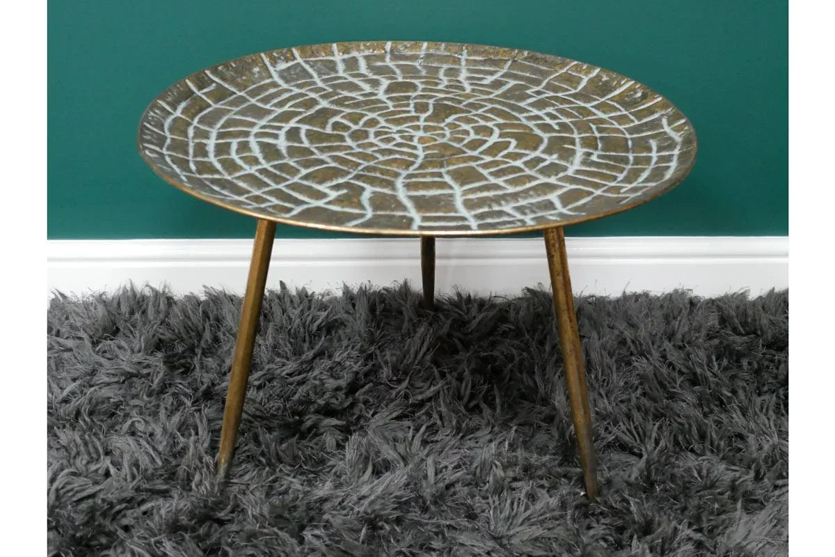 Round metal side table with textured top and three legs on a grey shaggy rug