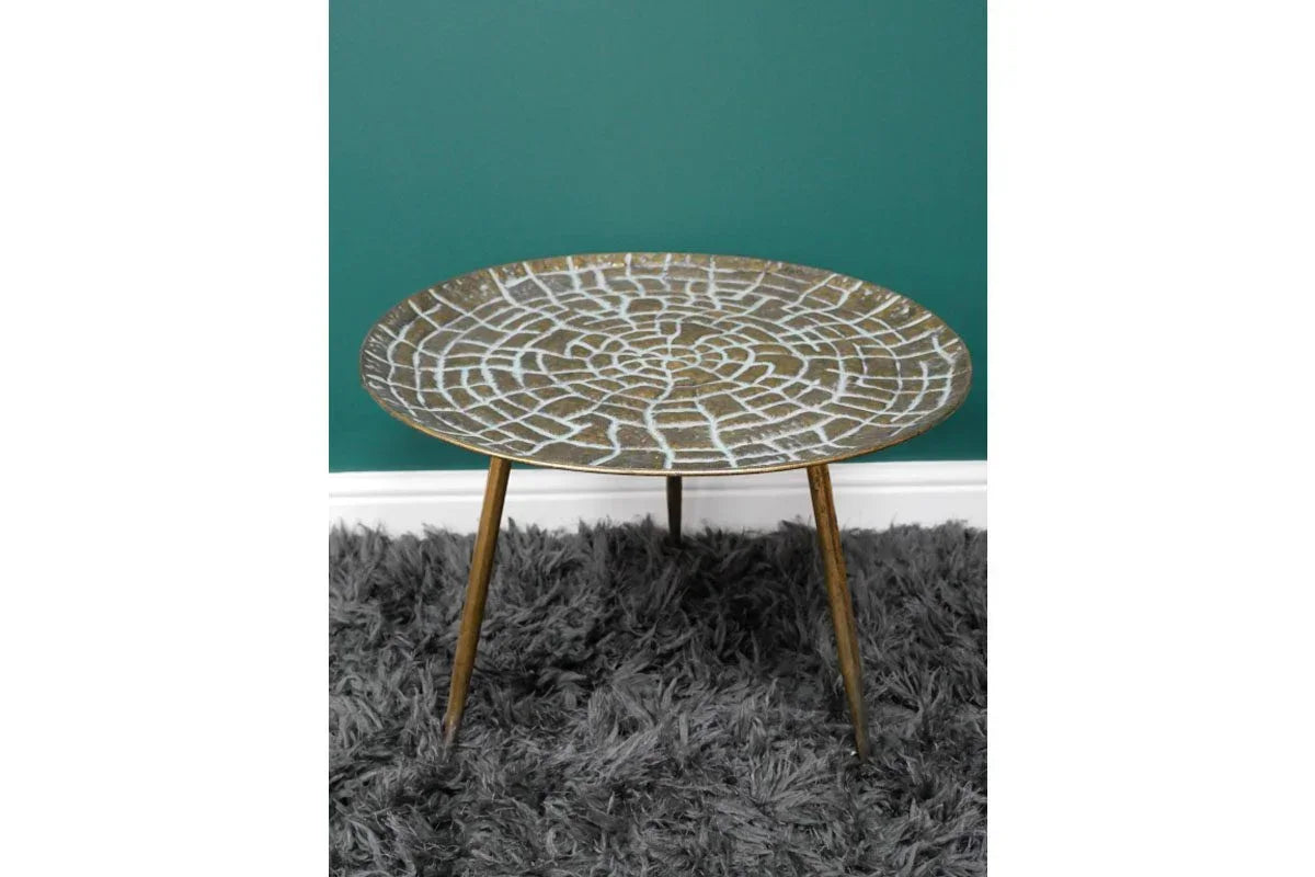 Round metal side table with textured gold top and three legs on a grey rug