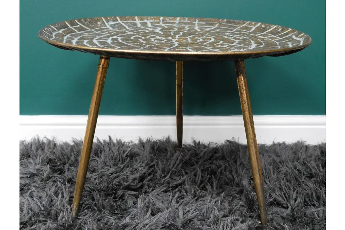 Round metal side table with leaf pattern top and gold tripod legs on grey rug