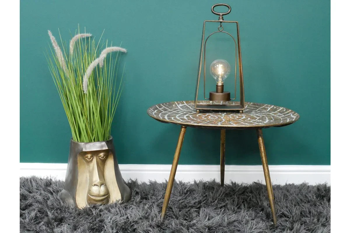 Round accent table with tripod legs beside decorative monkey face planter and grass