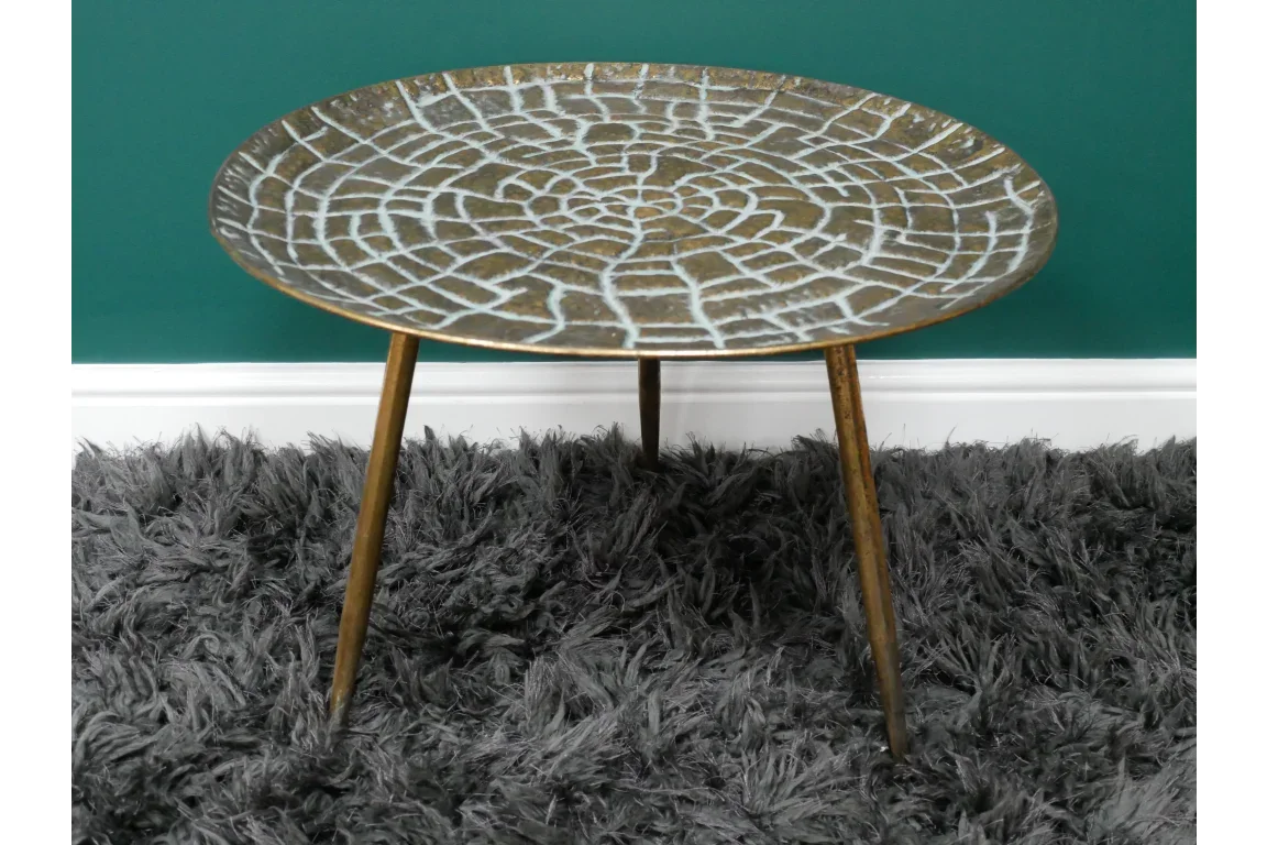 Round metal side table with textured bronze top and tripod legs on grey shaggy rug