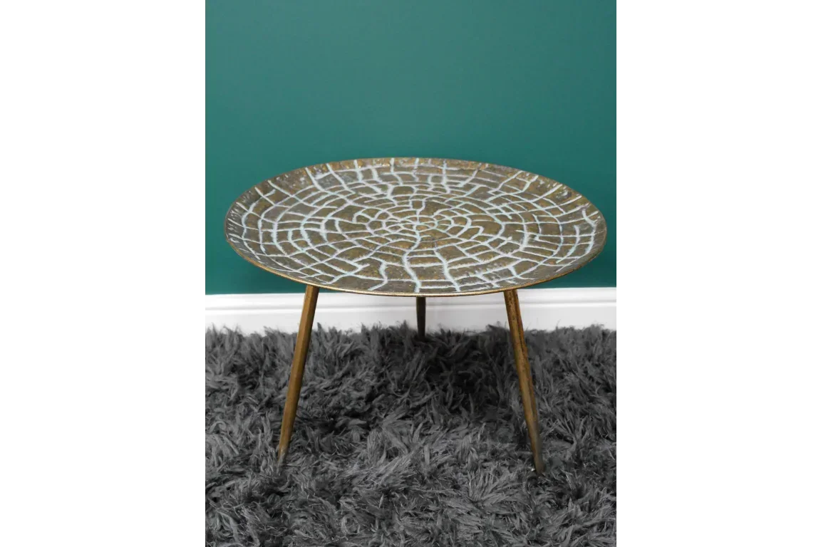 Round metal side table with gold finish and geometric pattern, angled on grey rug