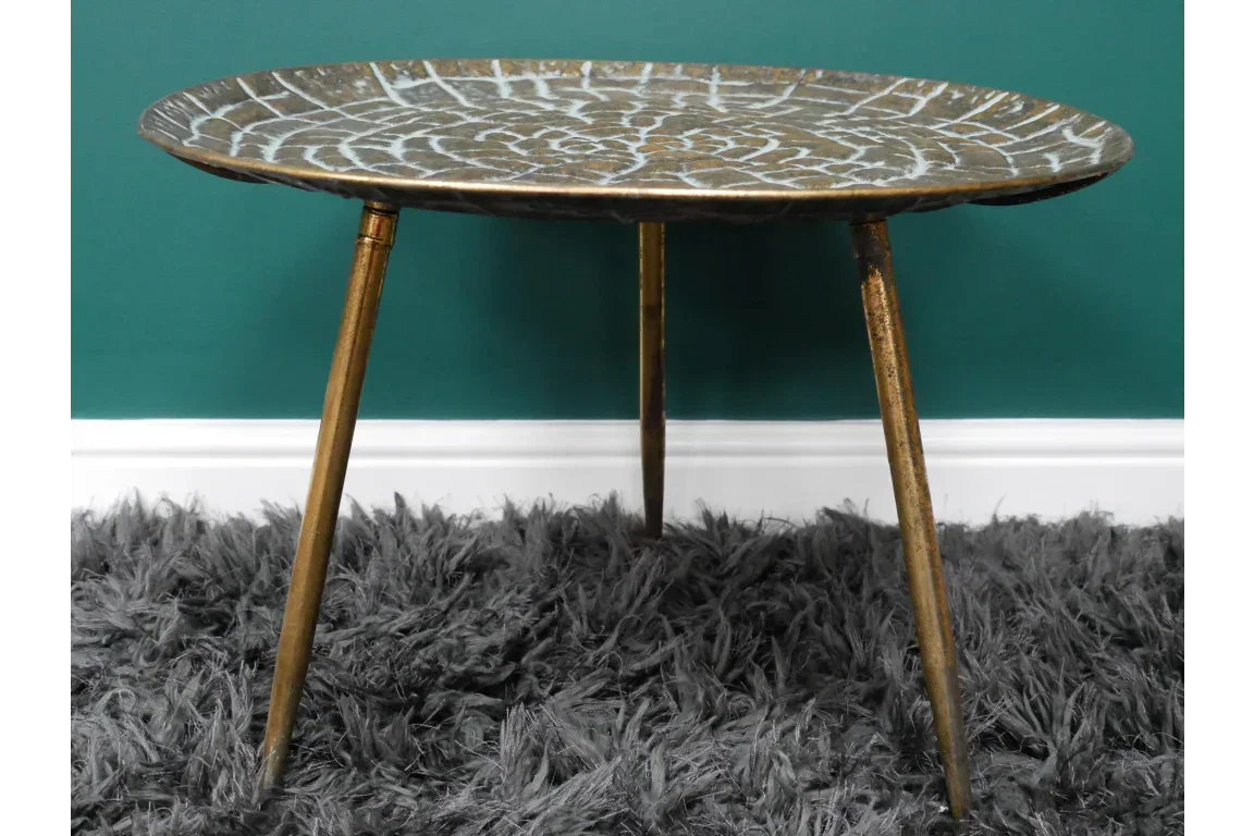 Metal side table with leaf pattern top and gold legs on grey shaggy rug