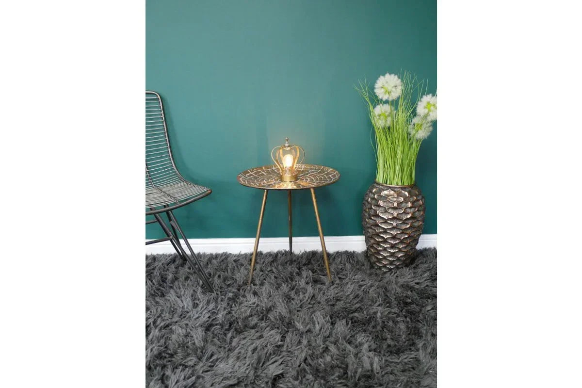 Bronze side table with crown ornament beside textured vase with artificial flowers on grey rug