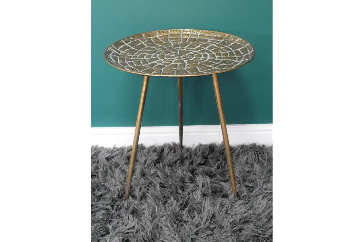 Round gold metal side table with mosaic top and tripod legs on grey shaggy rug