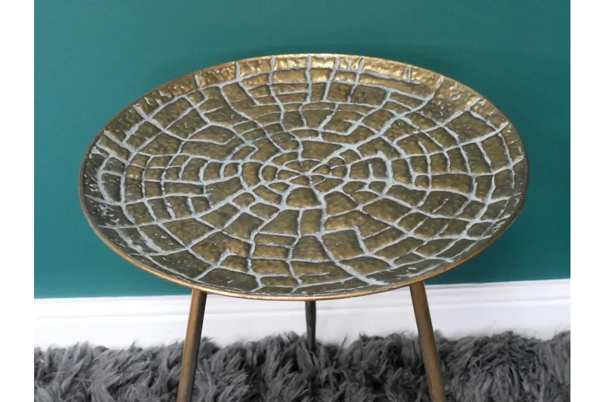 Round metal side table with textured bronze top and tripod legs on grey rug