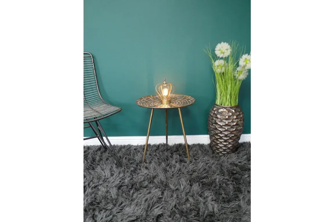 Gold accent side table with crown-shaped lamp next to metal chair and decorative vase