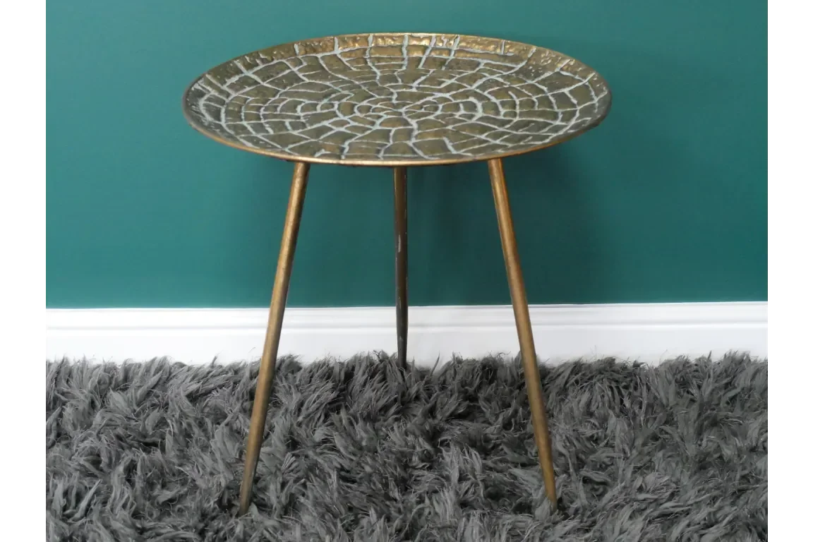 Round gold metal side table with textured mosaic top and three legs on a grey rug