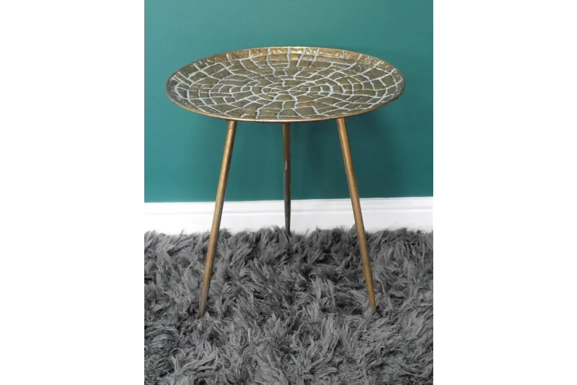 Round gold metal side table with textured top and tripod legs on grey shaggy rug