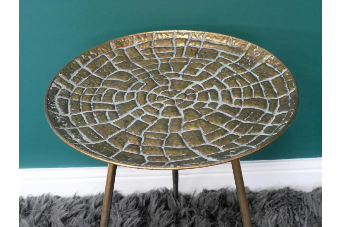Round metal accent table with textured gold top and tripod legs on a grey rug