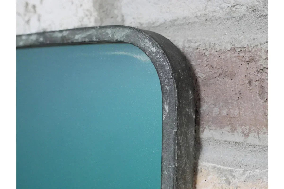 Close-up of metal-framed wall mirror corner with teal glass against brick wall