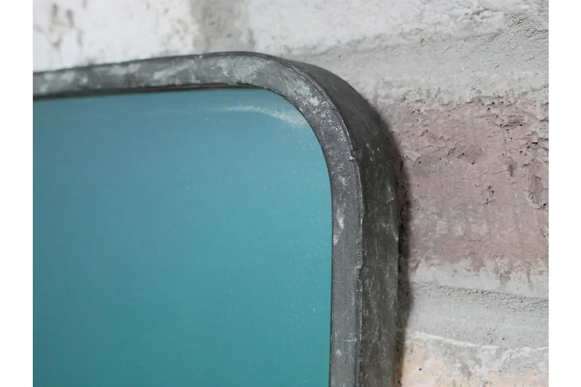 Closeup of metal framed wall mirror with teal glass against exposed brick wall