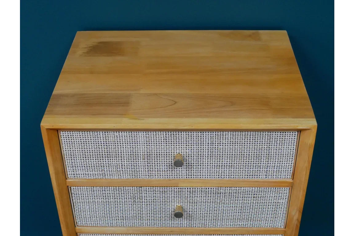 Wooden chest of drawers with cane front detail and brass knobs against teal wall