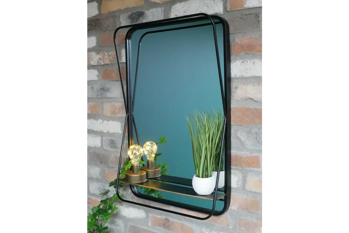 Rectangular wall mirror with black metal frame and shelf holding small plant and table lamps