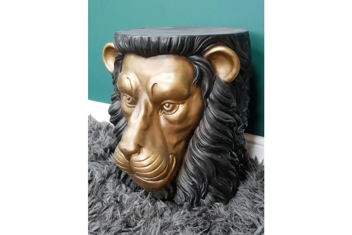 Gold lion head side table with black mane on grey textured rug against teal wall