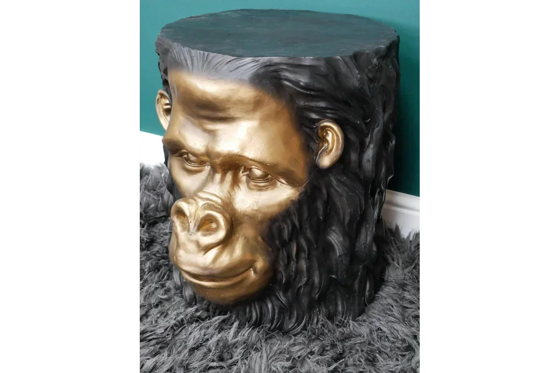 Black and gold gorilla head side table on grey shaggy rug against teal wall