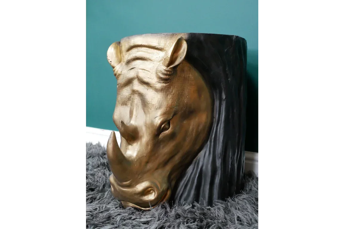 Gold rhinoceros head side table with textured details on plush grey rug against teal wall