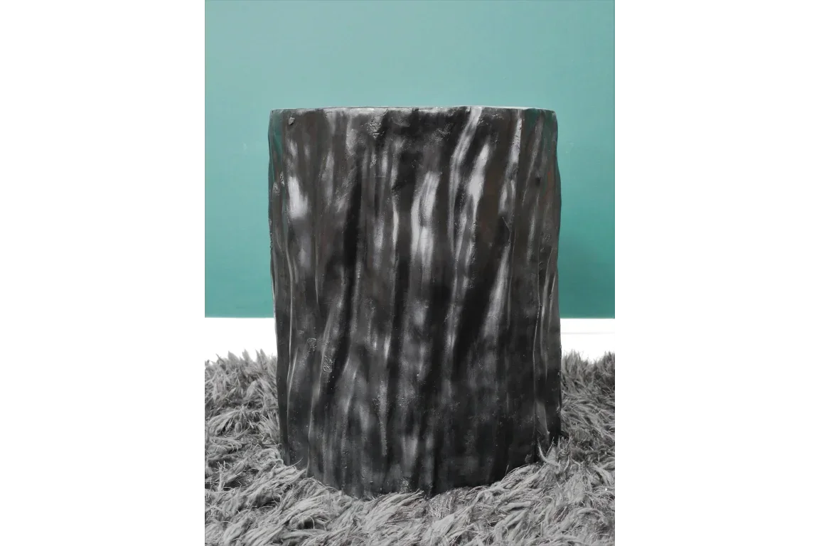 Black faux tree stump side table on grey shaggy rug against teal wall