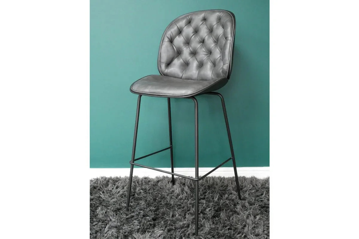 Grey bar stool with button-tufted backrest and black metal legs on a shaggy rug
